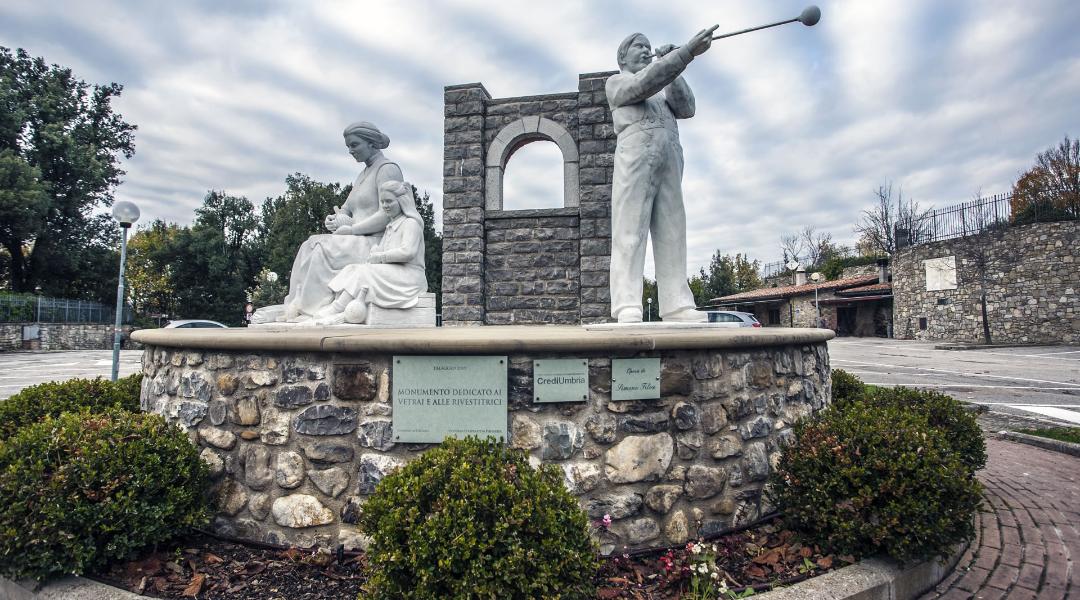 Stone monument dedicated to the glassmakers of Piegaro, with sculptures of a glassblower and two women coating flasks.