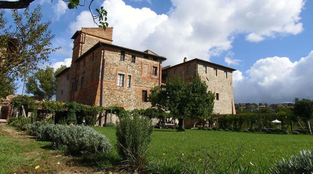 Abbey of the Seven Friars, a stone building surrounded by greenery, with a well-kept garden and a partially cloudy sky in the background.