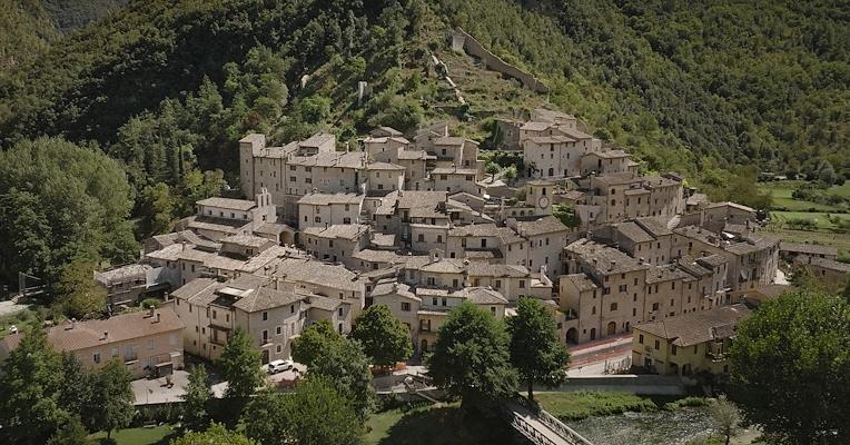 Veduta aerea di Scheggino, con case in pietra e una cinta muraria medievale, immerso nel verde della Valnerina.