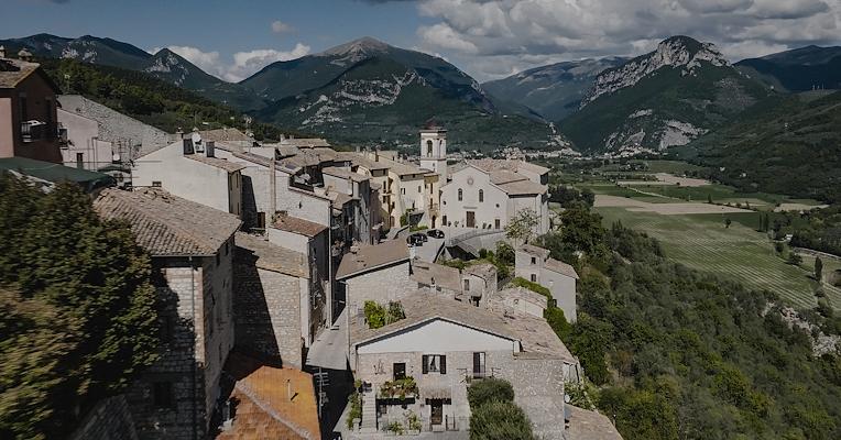 Veduta aerea di Montefranco, borgo umbro arroccato con chiesa centrale, tetti in pietra e monti verdi sullo sfondo.