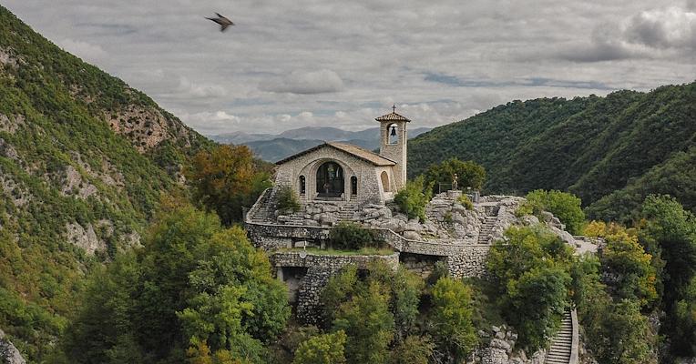 Veduta del Santuario di Roccaporena, incastonato tra le montagne umbre, con sentiero in pietra che sale tra la vegetazione.