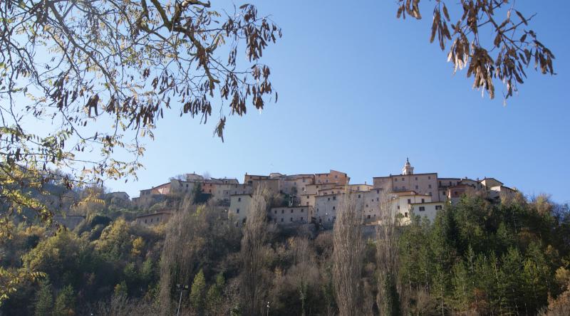 Panorama del borgo umbro di Preci, arroccato sul pendio e circondato da boschi, sotto un cielo limpido.