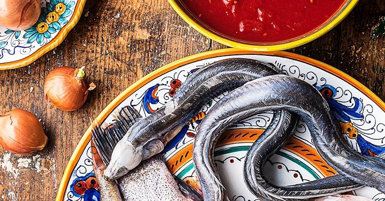 Eel and lake fish on a decorated plate, with onions and tomato sauce, on a rustic wooden table.
