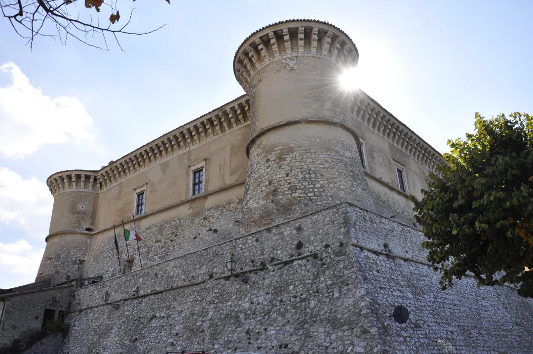 The Rocca of Alviano in the foreground, with battlemented towers and stone walls, lit by the sun behind its structures.