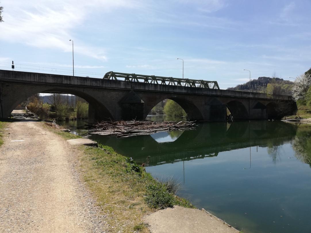 Sponda di un fiume con percorso ciclabile e ponte ferroviario