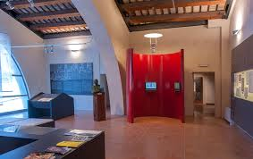 Museum hall with display cases, informational panels, a central red structure, and an exposed wooden beam ceiling.