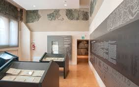 Museum hall with display cases, explanatory panels along the walls, and fragmented frescoes in the upper part.