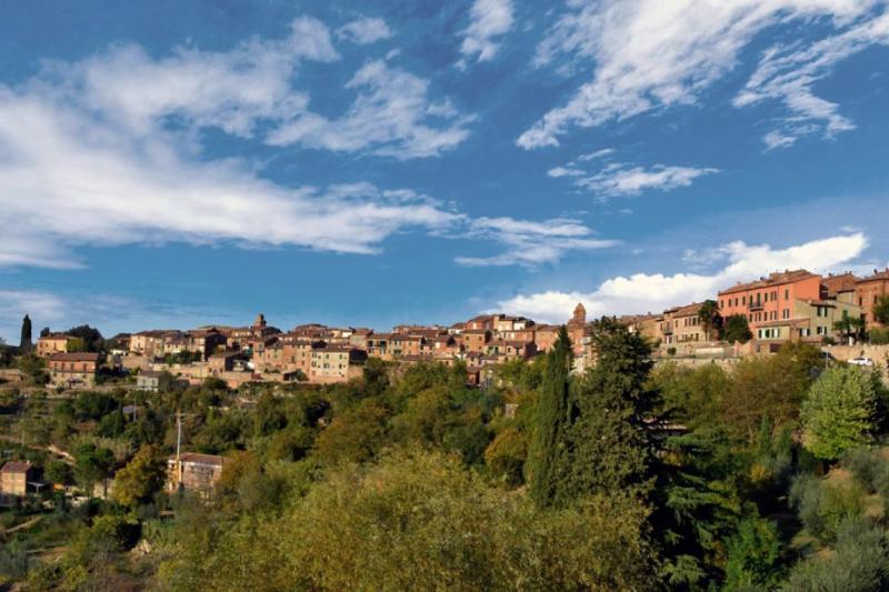 Veduta di Città della Pieve, borgo medievale in collina con edifici in mattoni e circondato da una vegetazione rigogliosa.