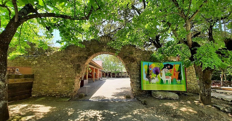 A stone archway among the trees leads into an amusement park; to its right, a giant book tells the story of the park.