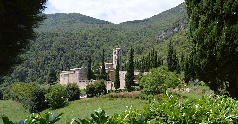 The Abbey of San Pietro in Valle surrounded by greenery, cypress trees, and wooded hills.