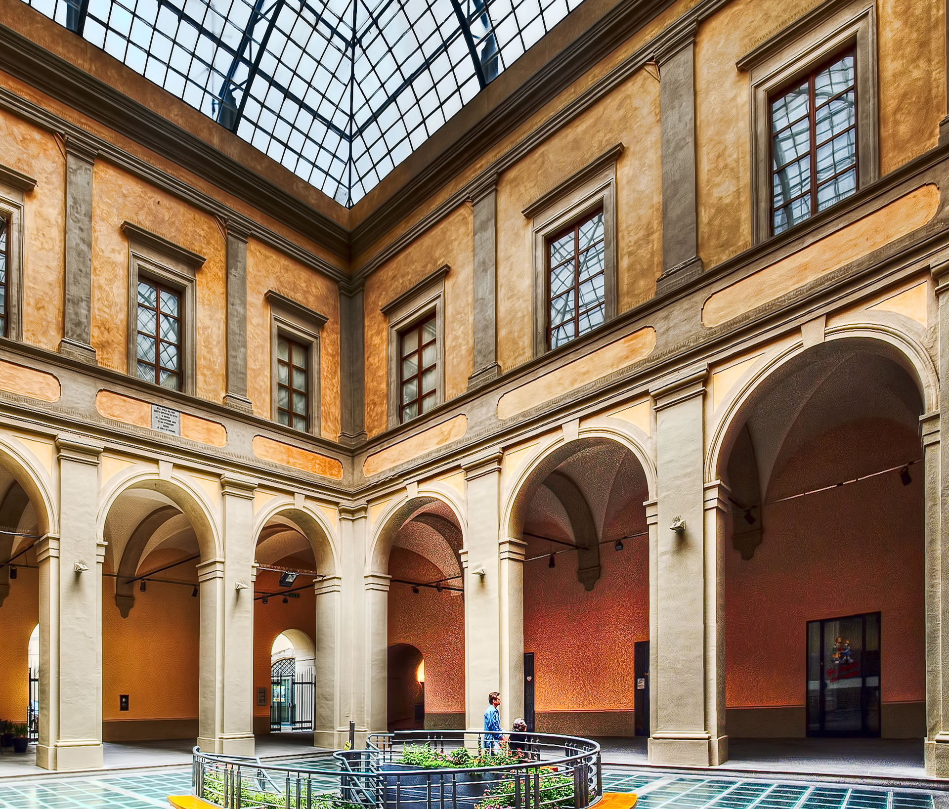 Inner courtyard of Palazzo Bufalini with an arcaded loggia, stone-framed windows and a glass roof.