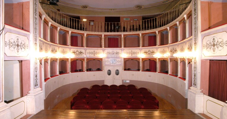 Interior of the Cesare Caporali Theatre in Panicale, with elegant decorated boxes and red seats.