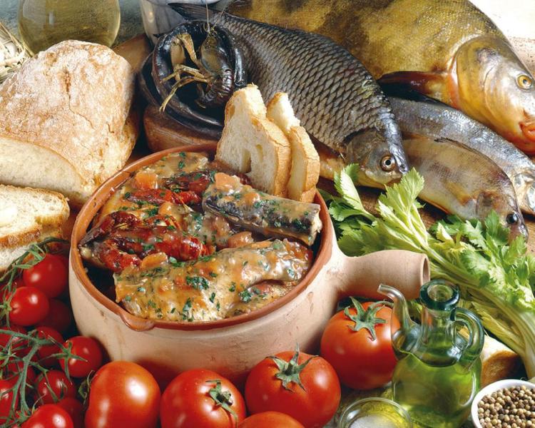 Piatto di pesce di lago in umido con pomodori, prezzemolo e pane, circondato da ingredienti freschi e pesci interi.