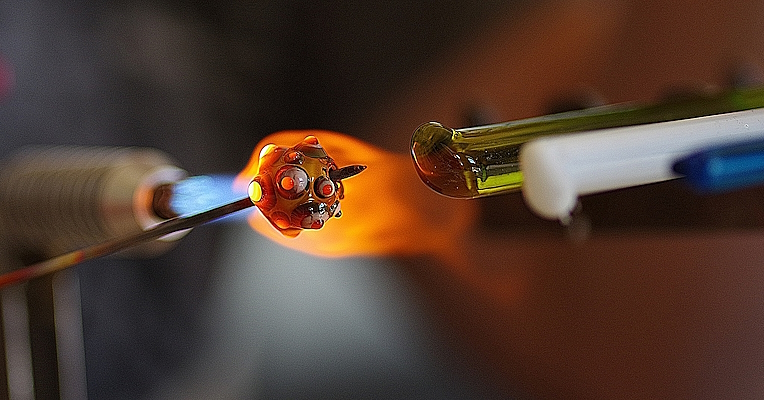 Baguettes de verre de différentes couleurs et une bille de verre fixée sur une tige métallique chauffée par le feu.