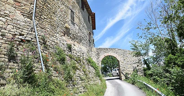 Entrée du bourg fortifié de Castel d’Arno, avec une route passant sous une arche en pierre entre les murs du château médiéval.