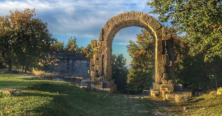 The view of the Arch of San Damiano, the monumental entrance to a decayed Roman city, nestled in the greenery of the Archaeological Park of Carsulae.