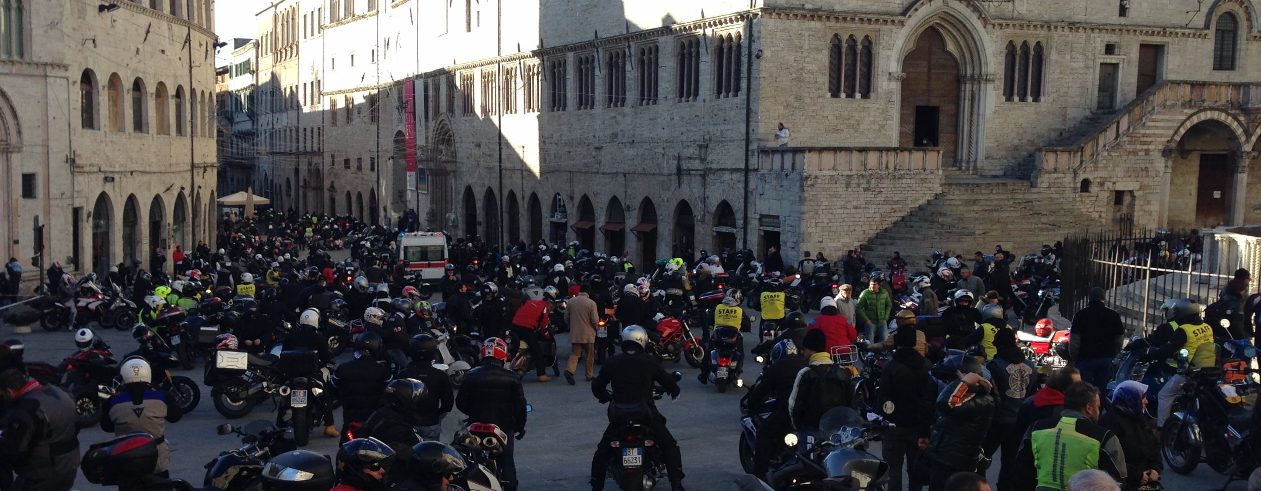 Piazza IV Novembre in Perugia crowded with motorcyclists and motorcycles during a rally; historic buildings in the background.