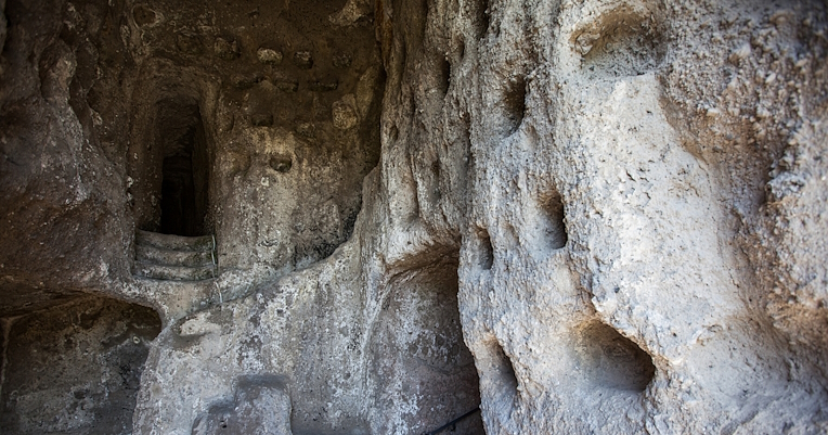 Rock wall with excavated cavities and a staircase leading to an internal passage in an ancient cave-like environment.