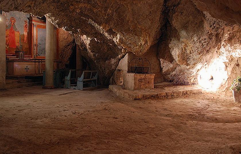 Interior of the cave of the Hermitage of Madonna del Riparo with frescoed altar, wooden benches and ancient stone well.