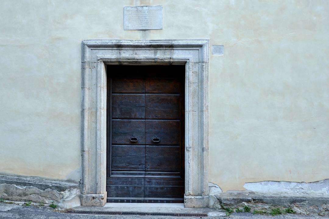 Stone portal with dark wooden door of the Sanctuary of Cancelli, set into the light plastered façade.