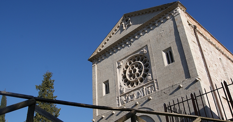 Romanesque façade of the Abbey of Saints Felix and Maurus in Castel San Felice, with carved rose window and clear sky.