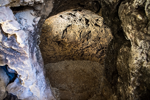 Small natural cave with irregular rocky walls and gravel-covered floor, lit by artificial light.