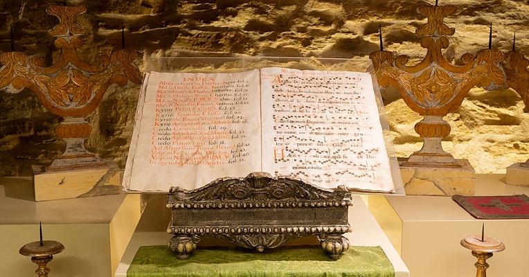 An antique music stand holding sheet music with liturgical hymns, showing visible notes and signs of wear from age.