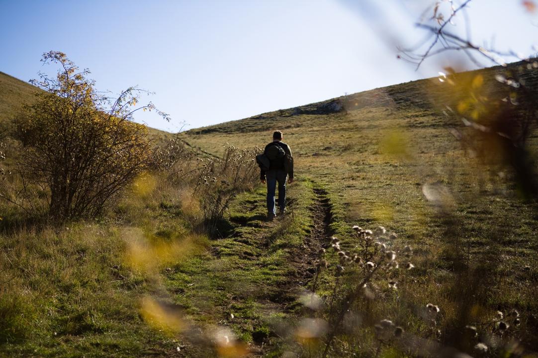 A man walks on open mountain terrain in Assisi with trekking gear