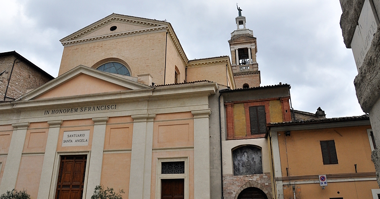 Façade de l'Église de San Francesco à Foligno avec clocher en arrière-plan, vue partielle des bâtiments adjacents.