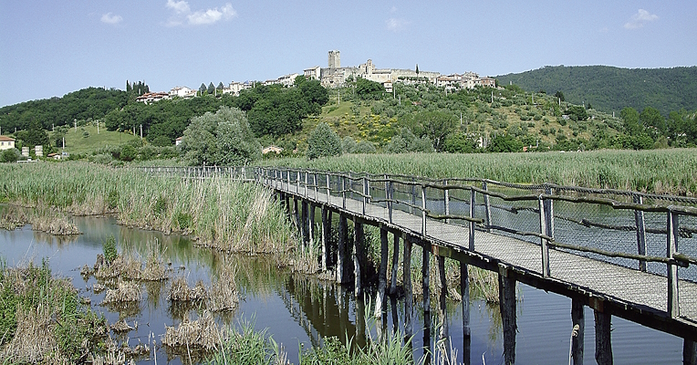 A bridge crosses the natural oasis, while the ancient medieval structures of the Castle of San Savino are visible atop the hill in the background.