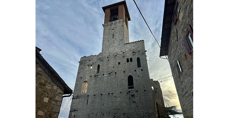Front facade of the Castle of Agello, characterized by ancient windows and dominated by a majestic bell tower towering over the building.