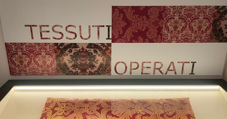 Image in the Figured Fabrics Room, featuring the Collicola Cushion in red and gold velvet in the display case