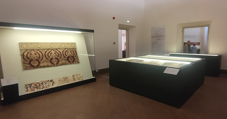 Interior of the sacred vestments room featuring the Antependium in red and gold displayed in a case and an altar frontal in the foreground