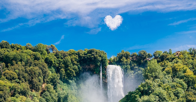 Cascade des Marmore avec une légère brume entourée de végétation. Dans le ciel, un nuage en forme de cœur