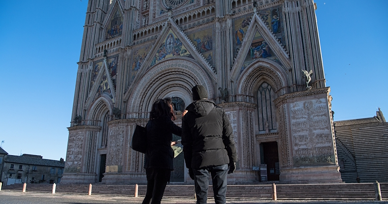 Deux personnes observent la façade de la cathédrale d’Orvieto qui se détache sous un ciel clair et serein