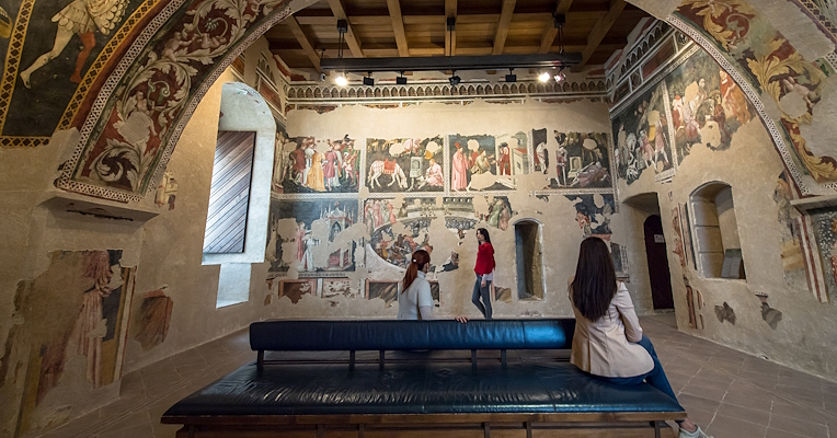 Intérieur de la Camera Pinta de la Rocca Albornoziana à Spolète, avec des visiteurs observant les murs décorés de fresques.