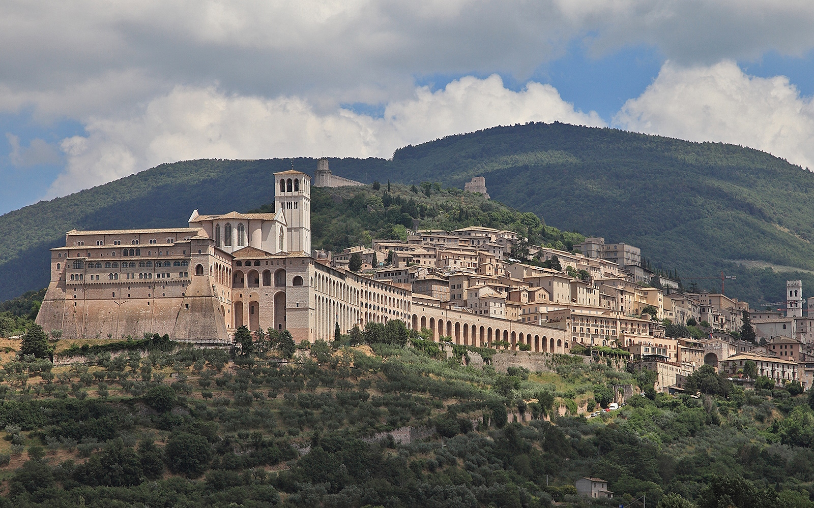 Panoramic view of Assisi featuring the Basilica of Saint Francis and historic buildings in the foreground, with Mount Subasio in the background