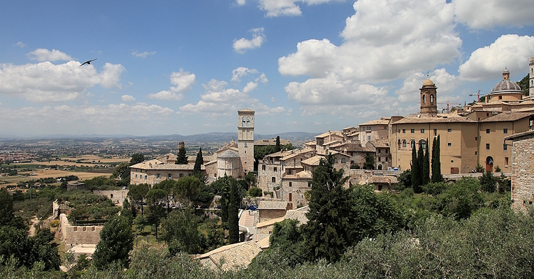Vue panoramique d’Assise avec les bâtiments historiques en pierre, les clochers et les tours sous un ciel clair avec quelques nuages