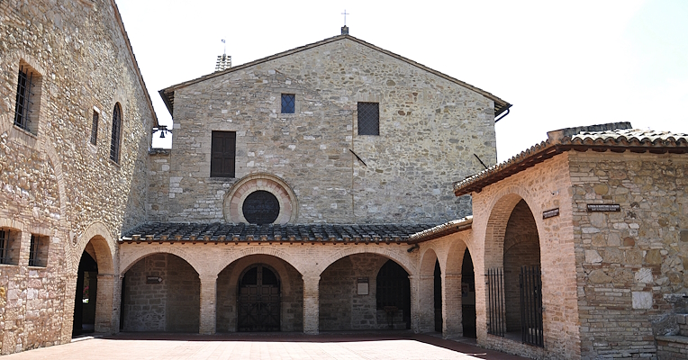 Place devant l’église San Damiano à Assise, avec une cour en pierre, des arcs et un portique en style médiéval.