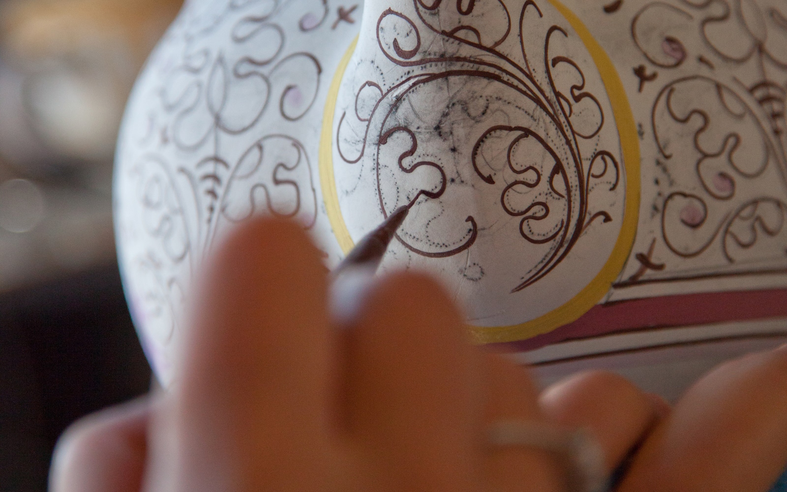 Ceramist hand-painting a vase with curved motifs and intricate details, tracing lines on a white surface