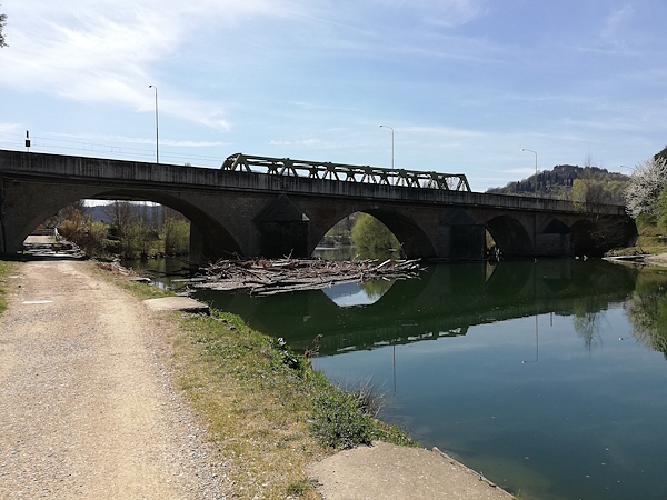 Sponda di un fiume con percorso ciclabile e ponte ferroviario