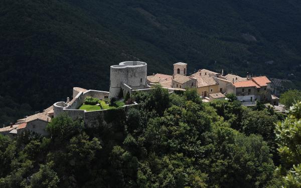  Aerial view of Polino, a medieval Umbrian village with a circular tower and fortified walls, surrounded by green forests. 