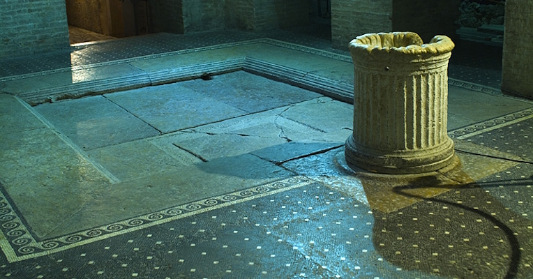 Interior of the Casa Romana in Spoleto with black and white mosaic floor, a central stone basin and a fluted column.