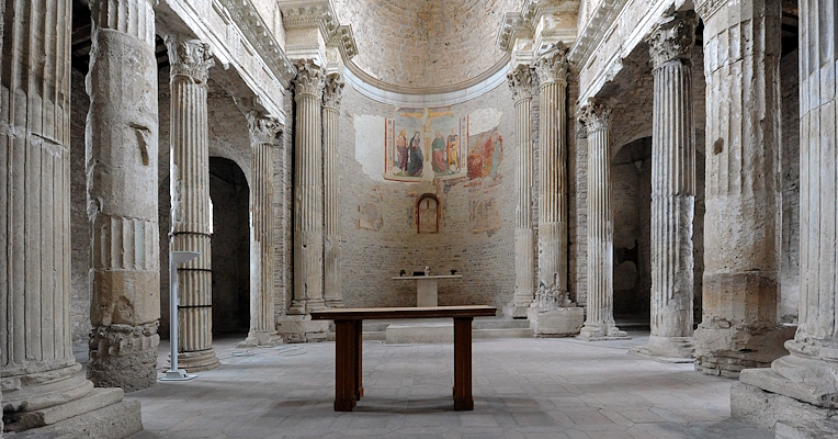 Interior of the Basilica of San Salvatore in Spoleto with Roman columns, an apse with frescoes and a central altar.