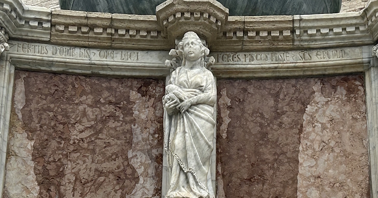 Scultura della Domina Lacii sulla Fontana Maggiore di Perugia, che ha in mano delle lasche, con iscrizioni latine sul marmo.