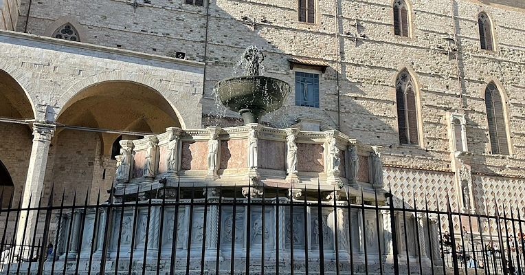 Fontana Maggiore di Perugia, con sculture in marmo, zampilli d'acqua e sfondo della Cattedrale di San Lorenzo.