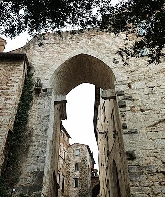 Porta Trasimena a Perugia, arco medievale in pietra incorniciato da edifici storici e rami di alberi sullo sfondo.