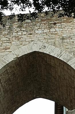 Detail of the Gothic arch of Porta Trasimena in Perugia, with exposed stone and a dace fish relief carved into the structure.