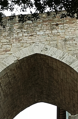 Dettaglio dell'arco gotico di Porta Trasimena a Perugia, con pietra a vista e rilievo di una lasca inciso sulla struttura.