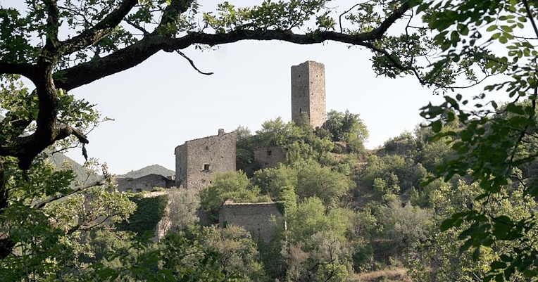 Ancienne tour de pierre sur une colline, entourée de ruines médiévales et d'une végétation luxuriante.